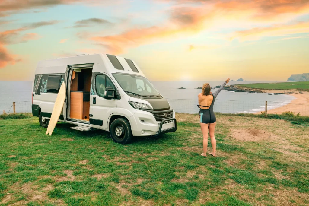 Young woman putting on her wetsuit for surfing next to her camper van